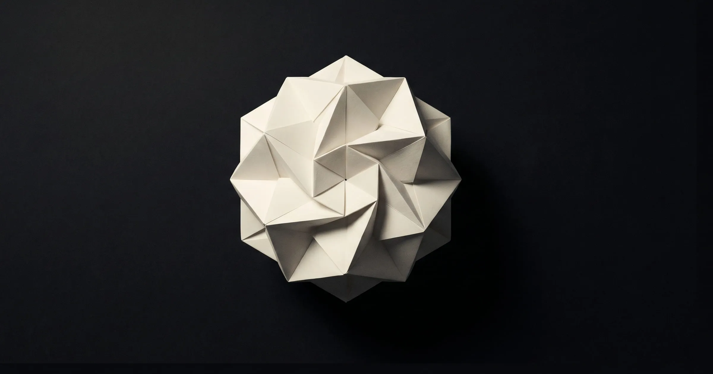 Hand-folded paper polyhedron with sharp triangular facets, suspended in matte black space — Field Notes header